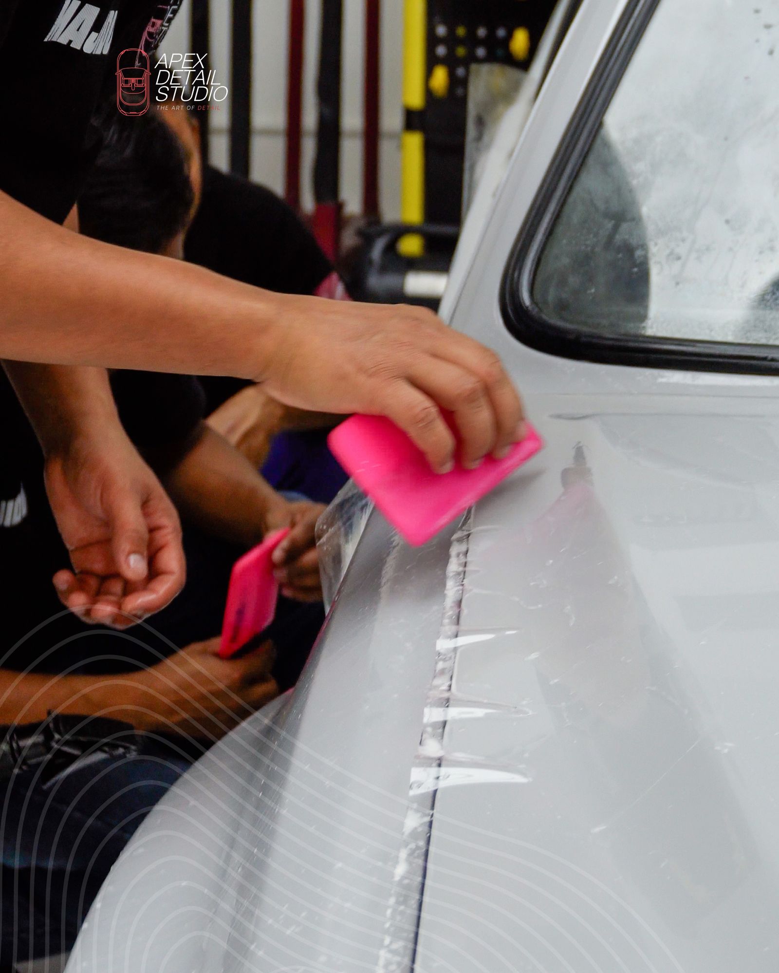 Two installers squeegeeing paint protection film on a grey car door at Apex Detail Studio Dubai