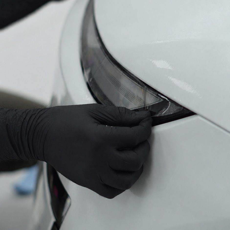 Installer wrapping PPF around a white car headlight edge at Apex Detail Studio Dubai