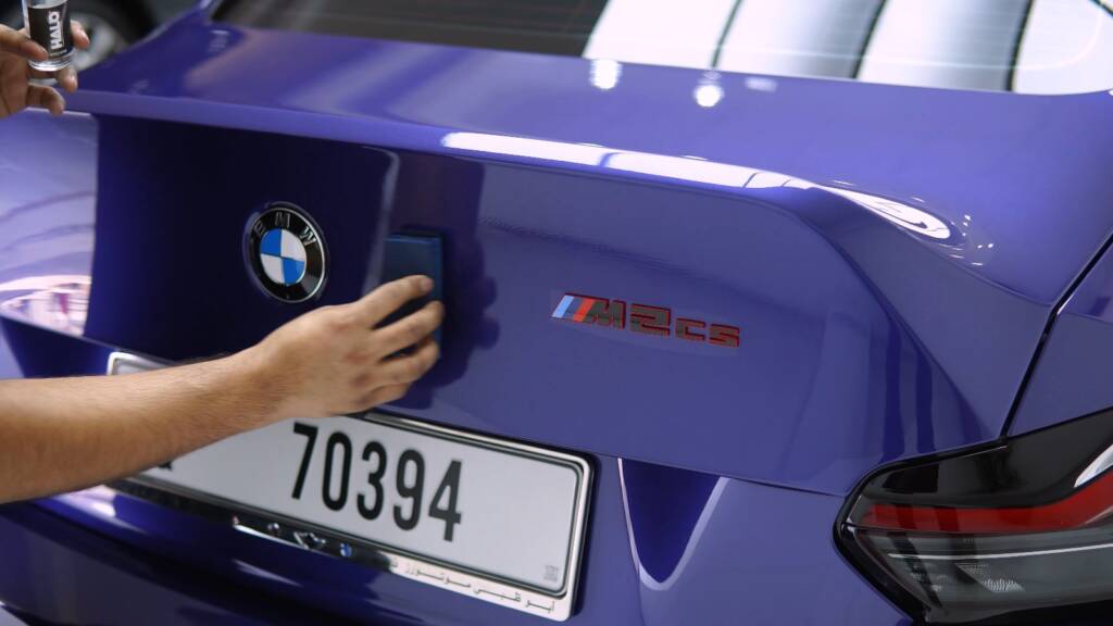 Detailer wiping the M2 CS badge on the boot of a blue BMW