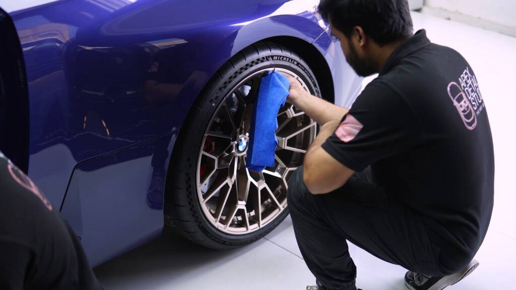 Detailer wiping the wheel of a blue BMW M2 CS