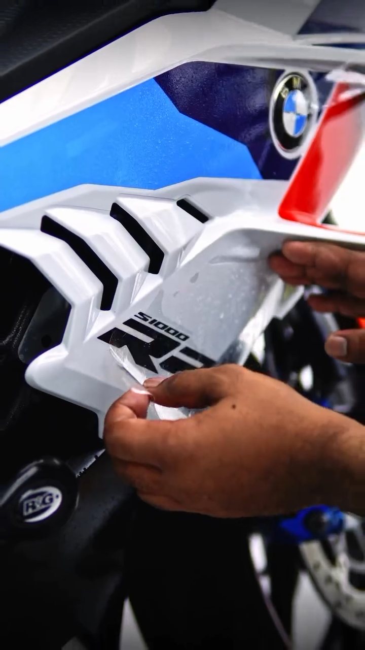 Hands wrapping PPF around the BMW S1000RR M livery fairing edge in Dubai