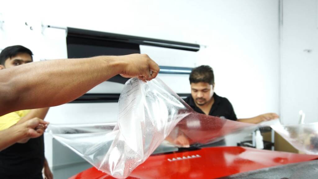 Installers lifting a large premium PPF sheet over a Ferrari Portofino