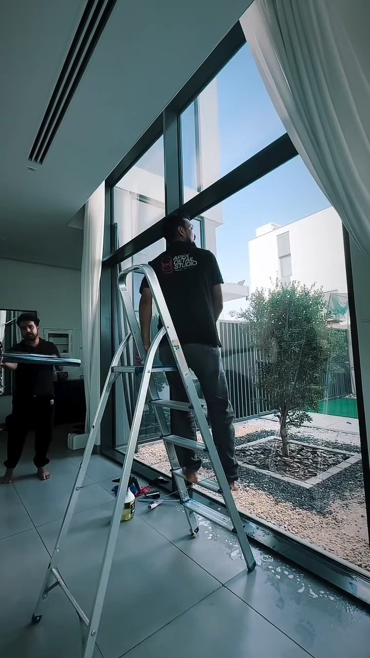Apex installer on a ladder fitting heat rejection film to a tall villa window in Dubai