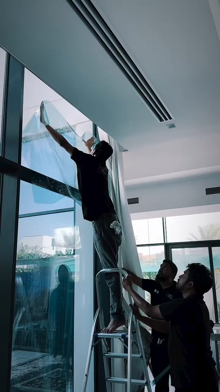 Two Apex installers working on high glass panels with home window film in Dubai