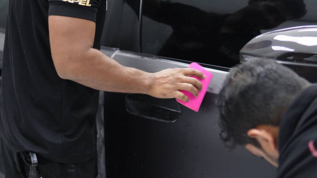 Two Apex installers squeegeeing matte PPF onto the door of a BMW M5 Touring