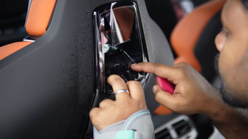 Installer applying clear PPF to the gloss seat back trim of a BMW M5 Touring with orange leather seats