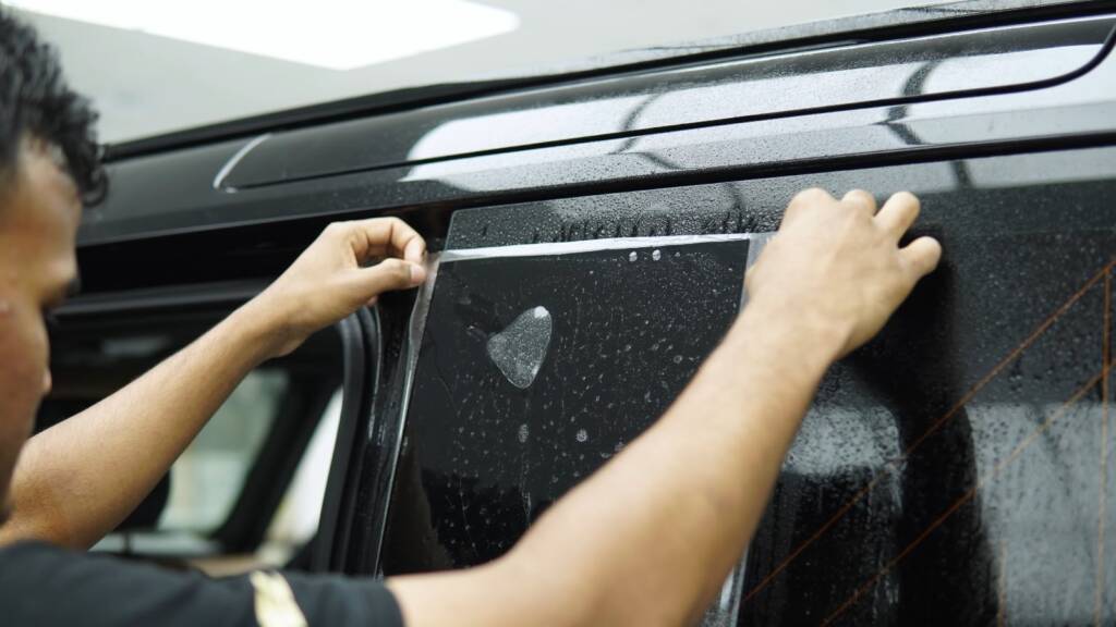 Two installers applying PPF to the rear side panel of a Land Rover Defender