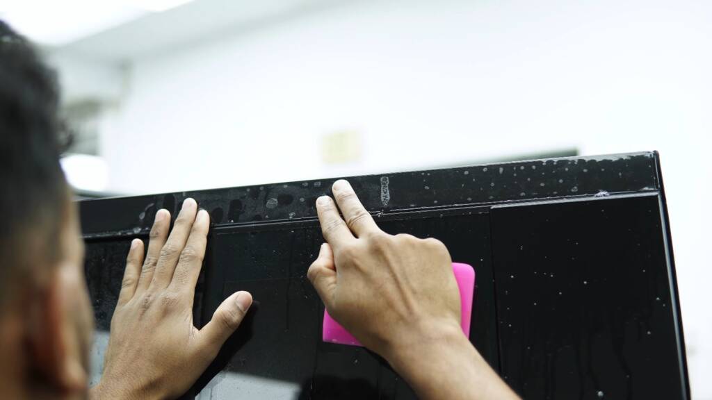 Squeegee pressing PPF onto a black Land Rover Defender panel in Dubai