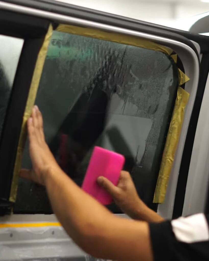 Installer squeegeeing tint on a 2026 Defender rear door glass, Apex Dubai