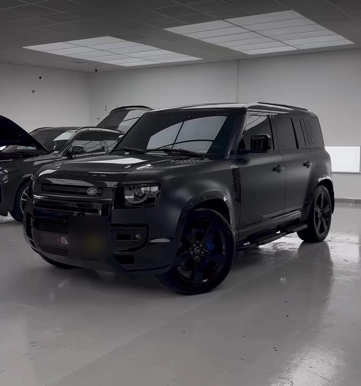 Front three-quarter view of a satin black Land Rover Defender with black painted wheels and side steps at Apex Detail Studio Dubai