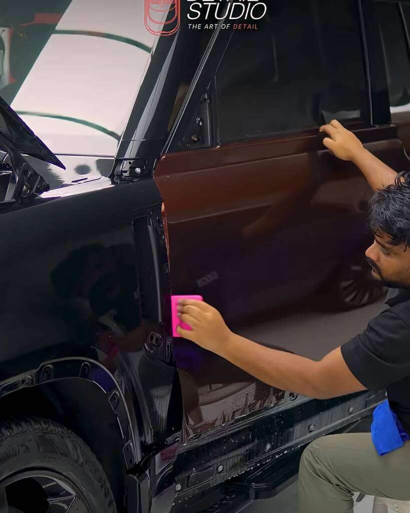 Installer squeegeeing Sedona Red colour PPF onto a Land Rover Defender door, Apex Dubai