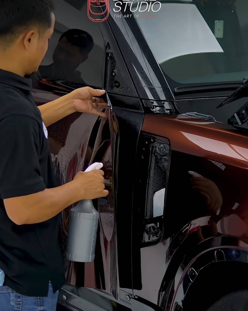 Installers laying Sedona Red colour PPF on a Land Rover Defender at Apex Dubai