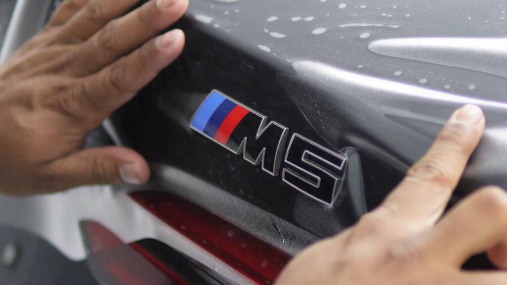 Matte PPF being smoothed around the M5 badge on the tailgate of a BMW M5 Touring