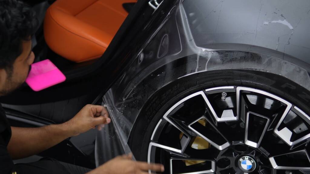 Installer applying matte PPF along the rear wheel arch of a BMW M5 Touring