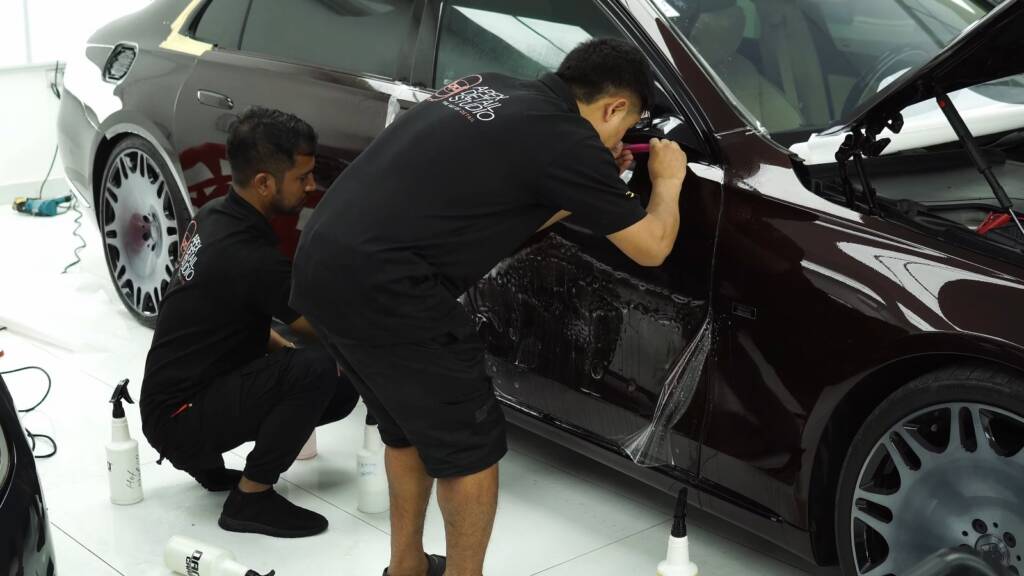 Two installers fitting PPF to the lower panels of a Maybach S680