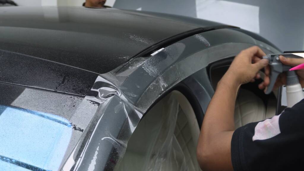 Installer stretching PPF around the rear wing of a grey Mercedes S500