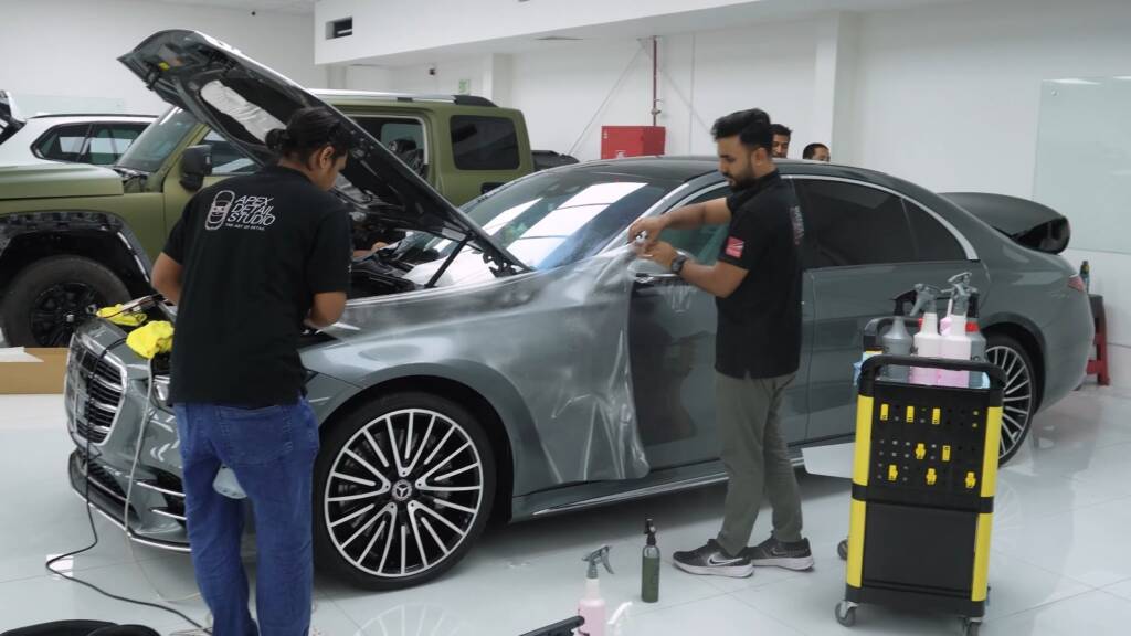 Two installers wiping down the side of a grey Mercedes S500 before paint protection film