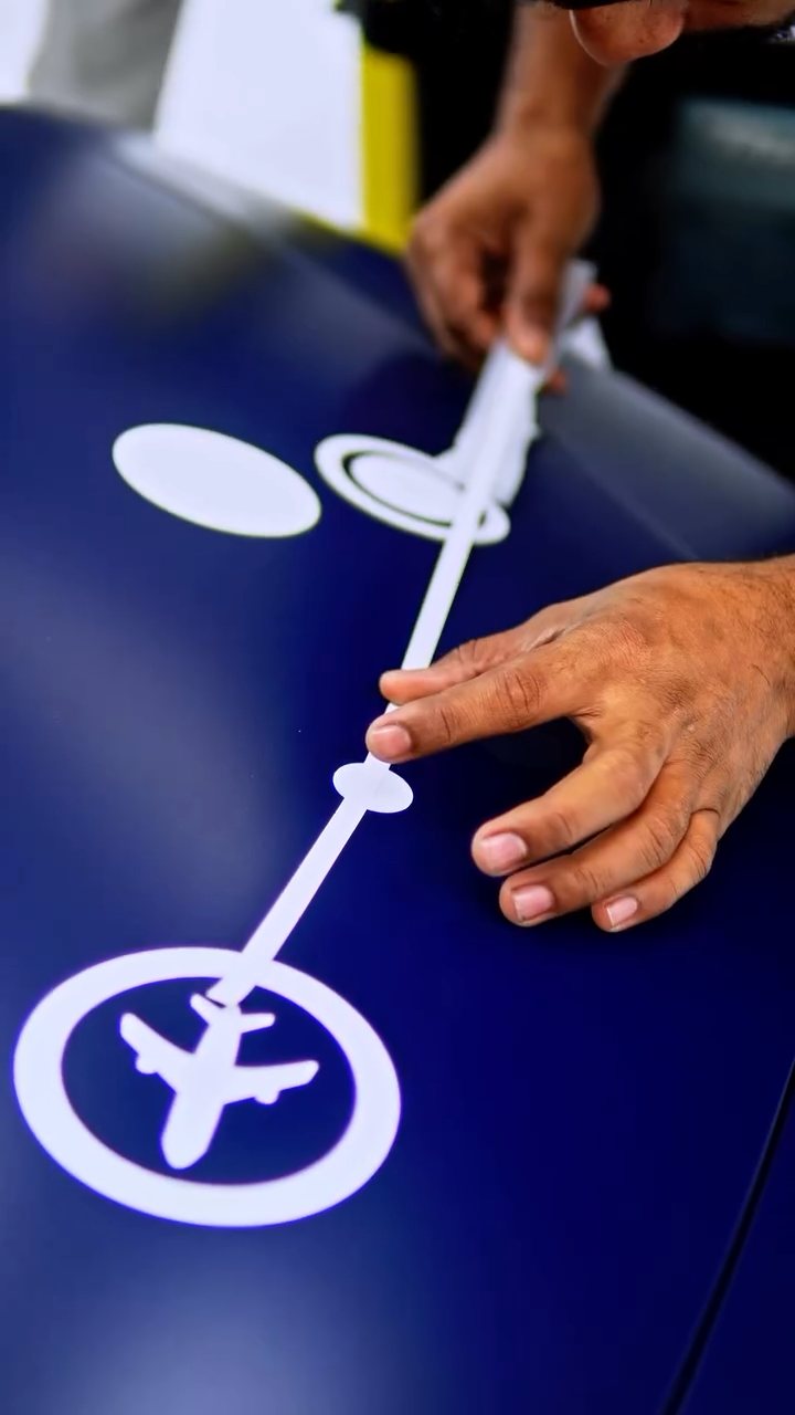 Installer applying a white livery decal to the blue Nissan Z at Apex Detail Studio