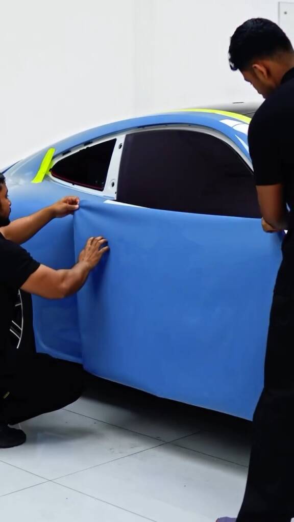 Two installers laying blue colour PPF across the door of a Porsche 911 Carrera in Dubai