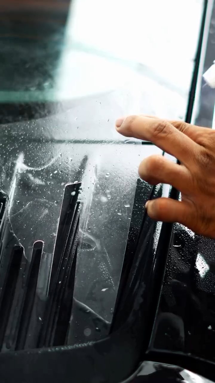 Hands pressing PPF between the Porsche 911 Carrera grille slats
