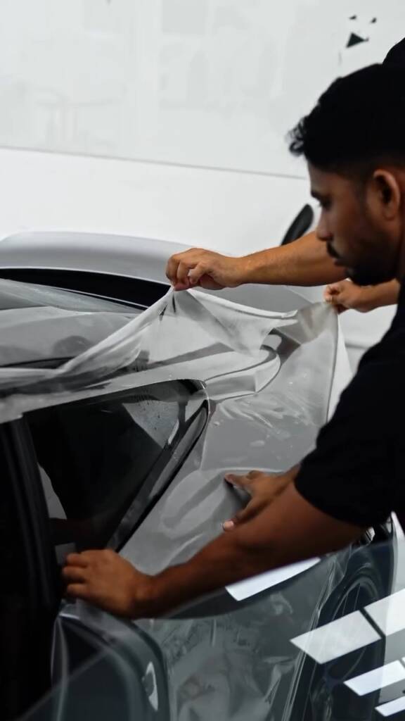 Two installers stretching one sheet of PPF around the rear pillar of a Porsche 911 GTS