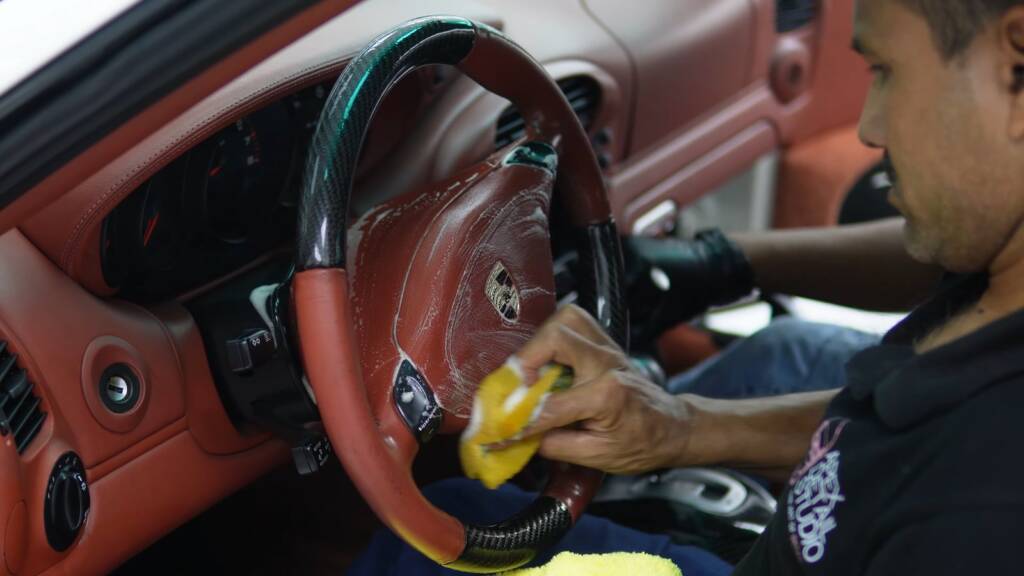 Detailer cleaning the steering wheel of a Porsche 996 Turbo with red interior