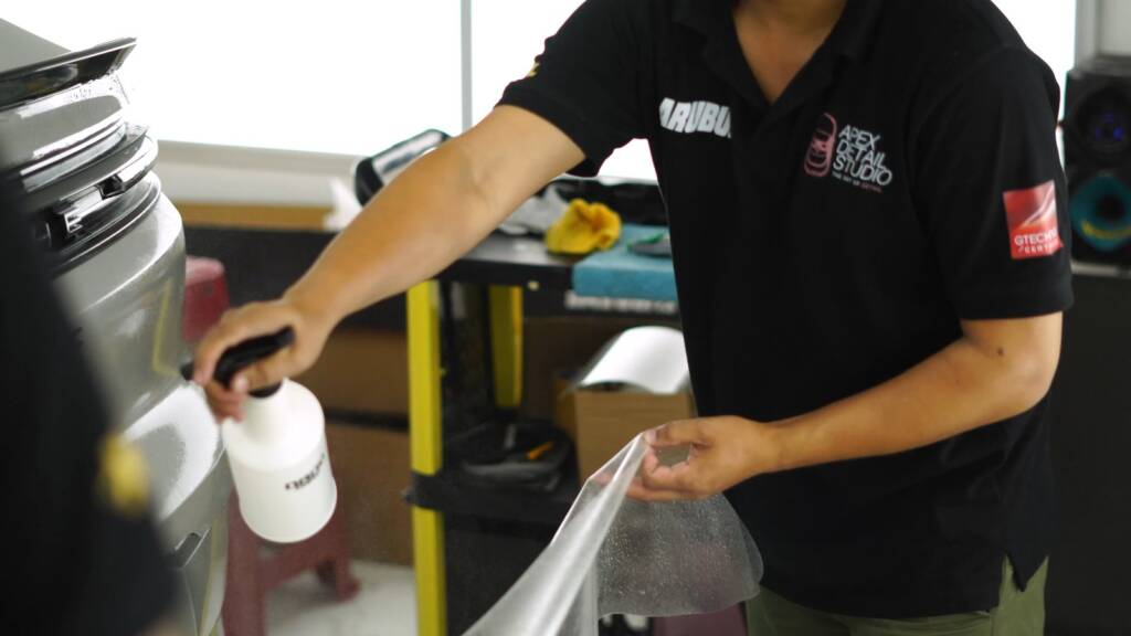 Installer spraying a panel of a Porsche Cayenne GTS during PPF