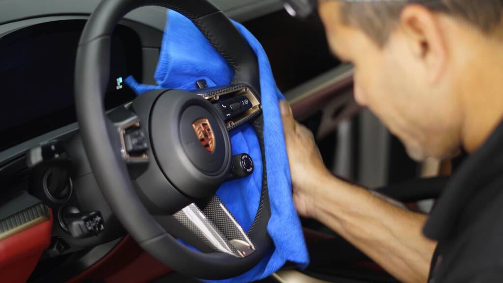 Detailer cleaning the steering wheel controls of a Porsche Cayenne GTS