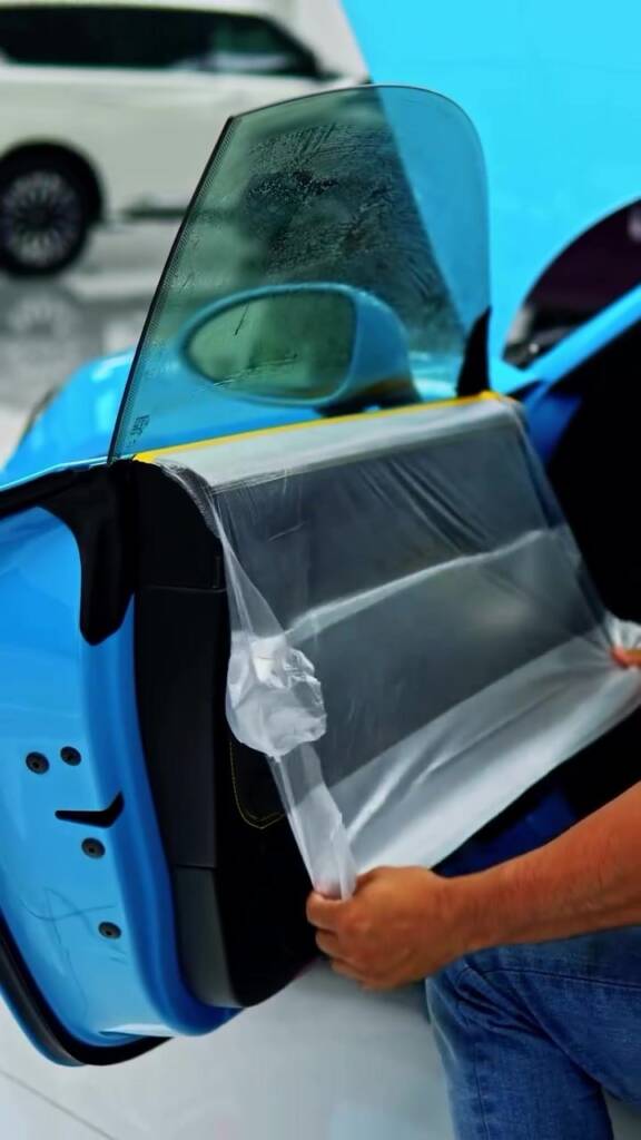 Installer preparing window tint film on the door of a blue Porsche Cayman GT4