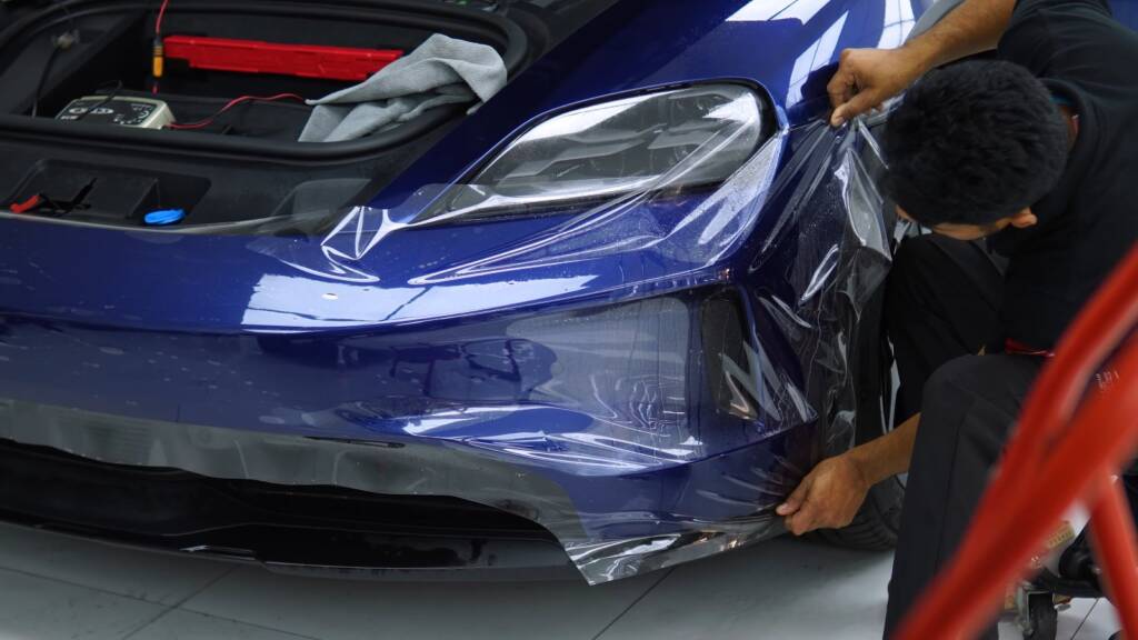 Installer fitting PPF to the front bumper of a Porsche Taycan