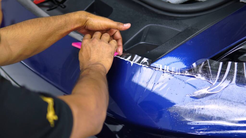 Installer working PPF around the front wing edge of a Porsche Taycan