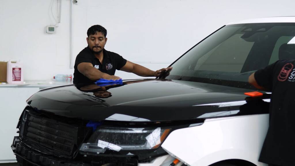 Installer laying gloss black colour PPF across the bonnet of a white Range Rover