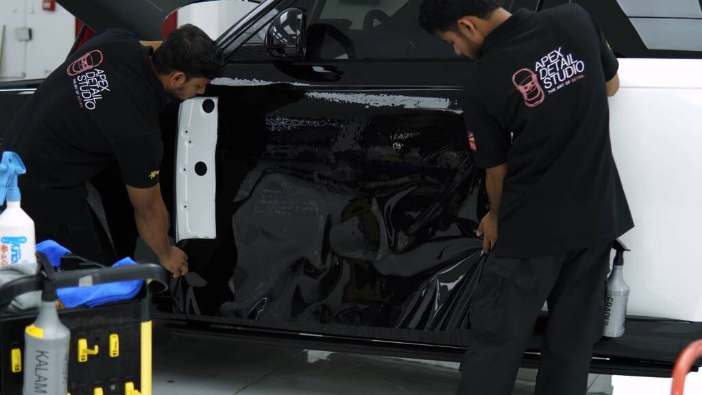 Installers working gloss black colour PPF along the side of a Range Rover