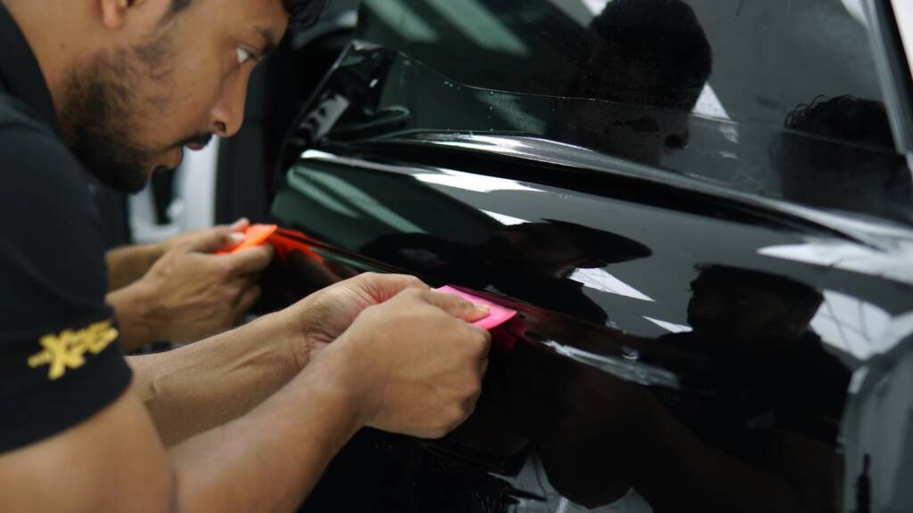 Two installers squeegeeing gloss black colour PPF on a Range Rover