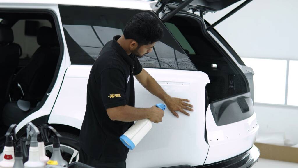 Installer spraying slip solution on the tailgate of a white Range Rover