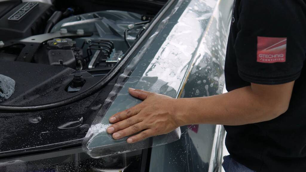 Installer wrapping clear PPF at the bonnet edge of a Rolls-Royce Ghost