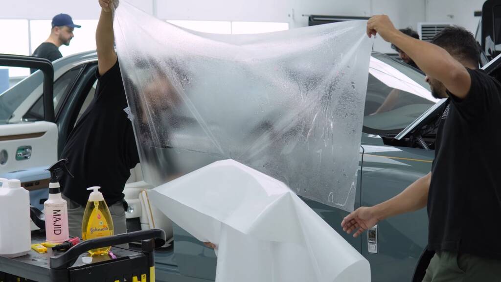 Apex installers handling a large sheet of PPF for a Rolls-Royce Ghost