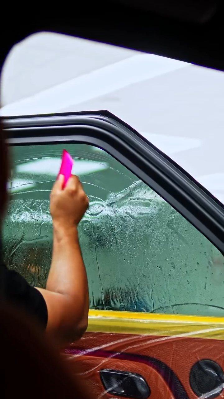 Pink squeegee pushing water out of the ROX Adamas tint at Apex Detail Studio