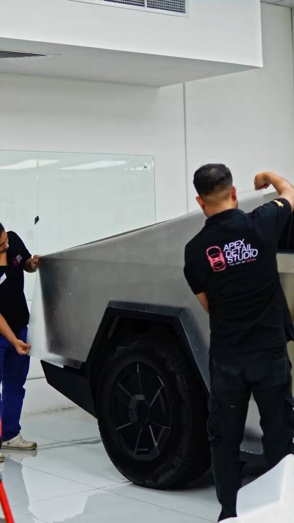 Three installers handling a full side panel of PPF on a Tesla Cybertruck