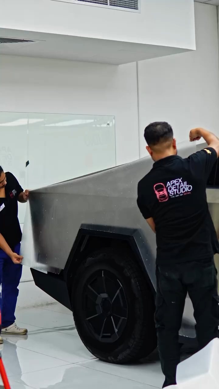 Three installers fitting a large PPF sheet to the Cybertruck stainless side panel