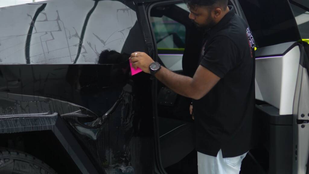 Installer working gloss black paint protection film across the rear door of a Tesla Cybertruck