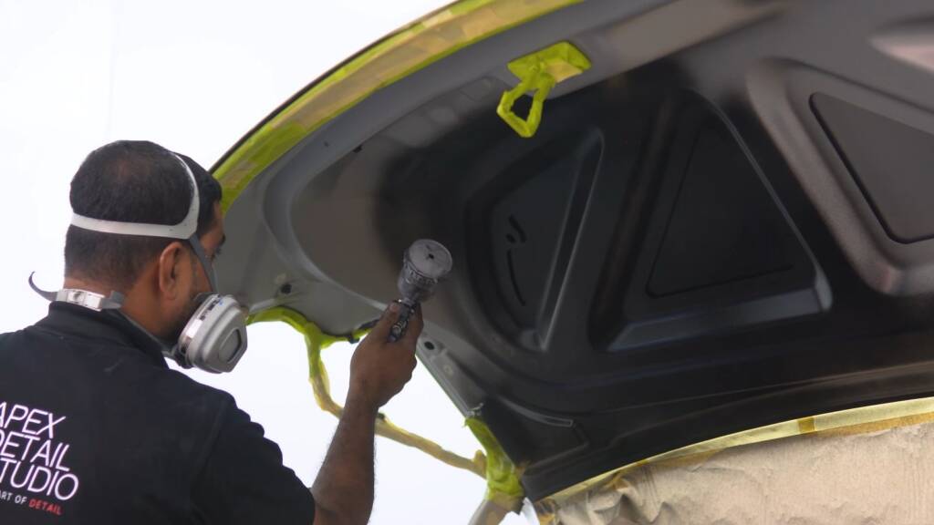 Technician spraying the inside of a Tesla Cybertruck tailgate with gloss black peelable paint