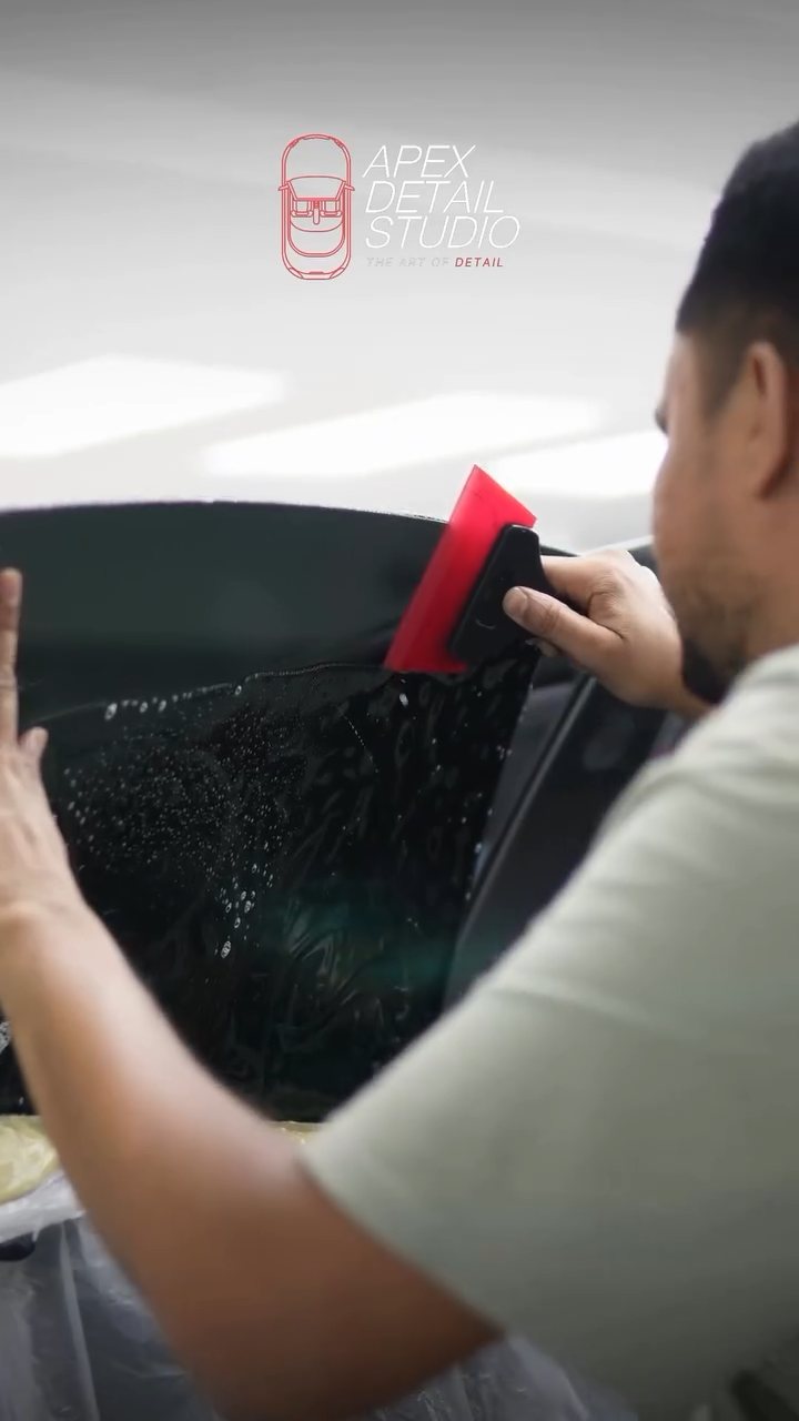 Installer squeegeeing window tint on the Tesla Model 3 glass at Apex Detail Studio Dubai