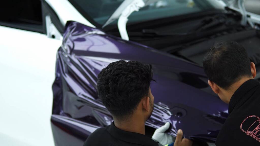 Two installers wrapping a Tesla Model Y Juniper front wing in purple