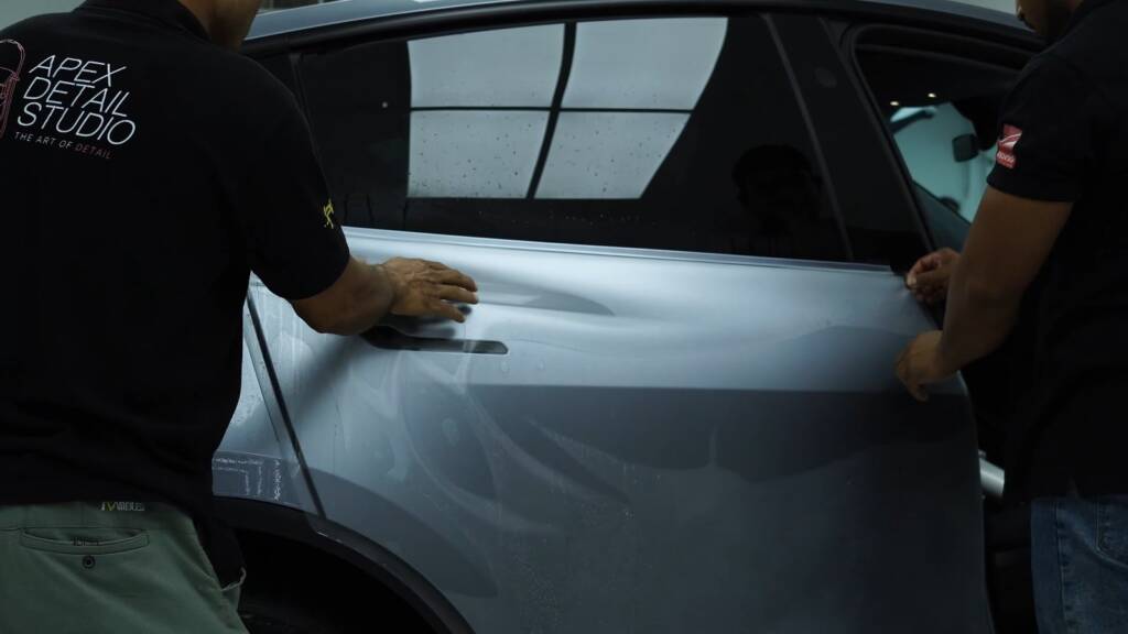 Two installers fitting stealth PPF to a Tesla Model Y Juniper door