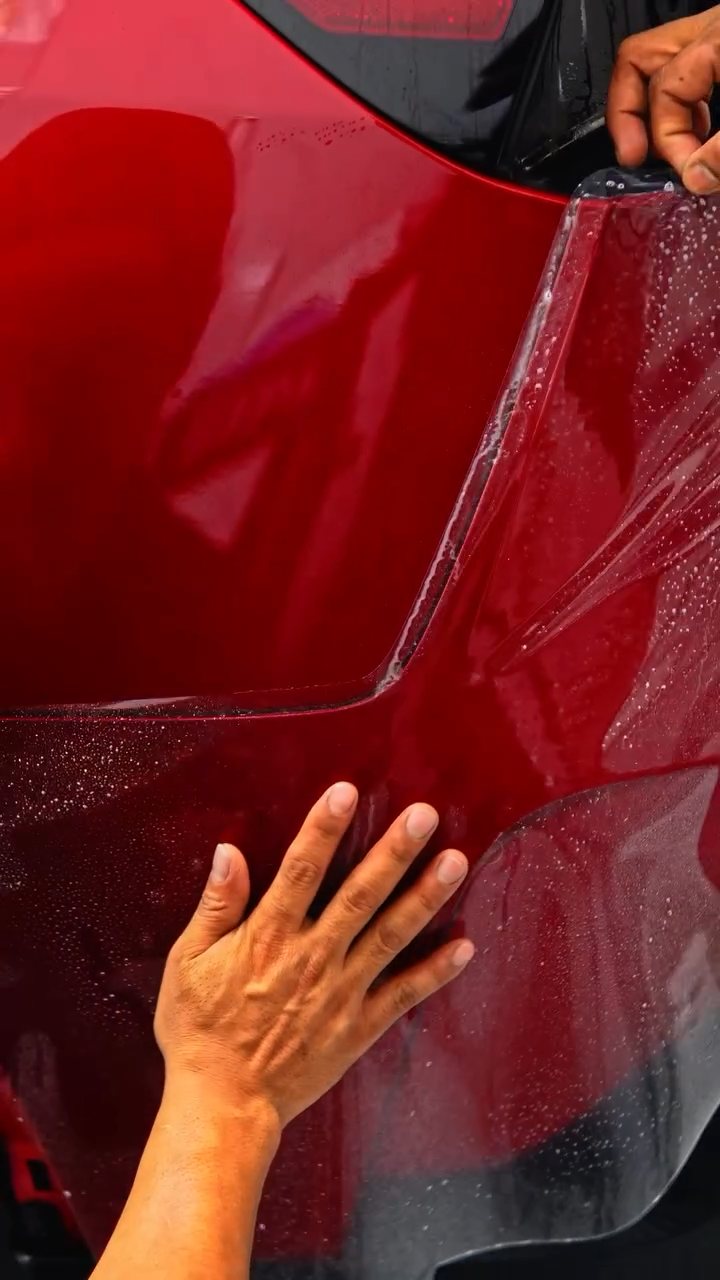 Hands smoothing PPF onto the Tesla Model Y Performance door at Apex Detail Studio