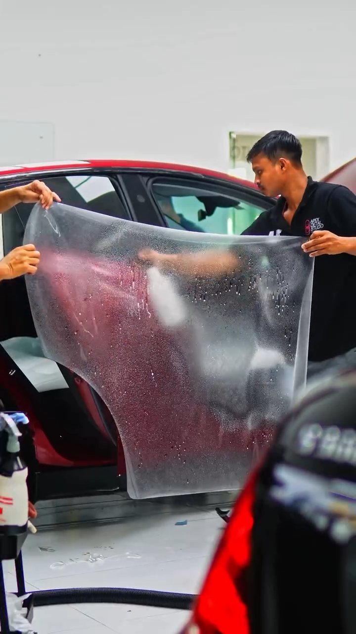 Two installers holding a full sheet of PPF for the red Tesla Model Y
