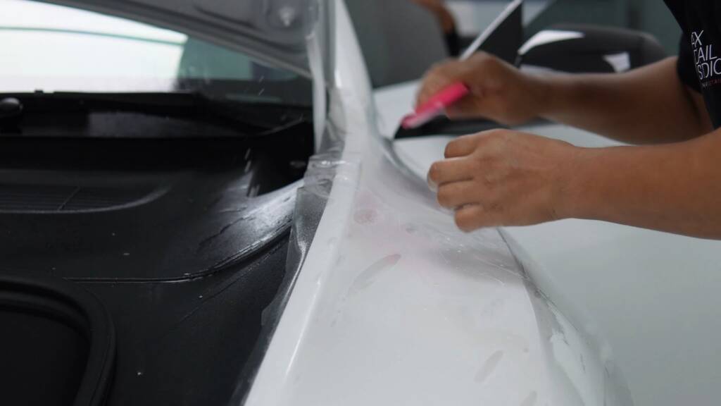 Installer tucking satin PPF around the boot opening of a white Tesla Model Y Performance