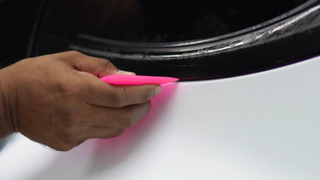 Installer squeegeeing satin PPF on the front bumper of a white Tesla Model Y Performance