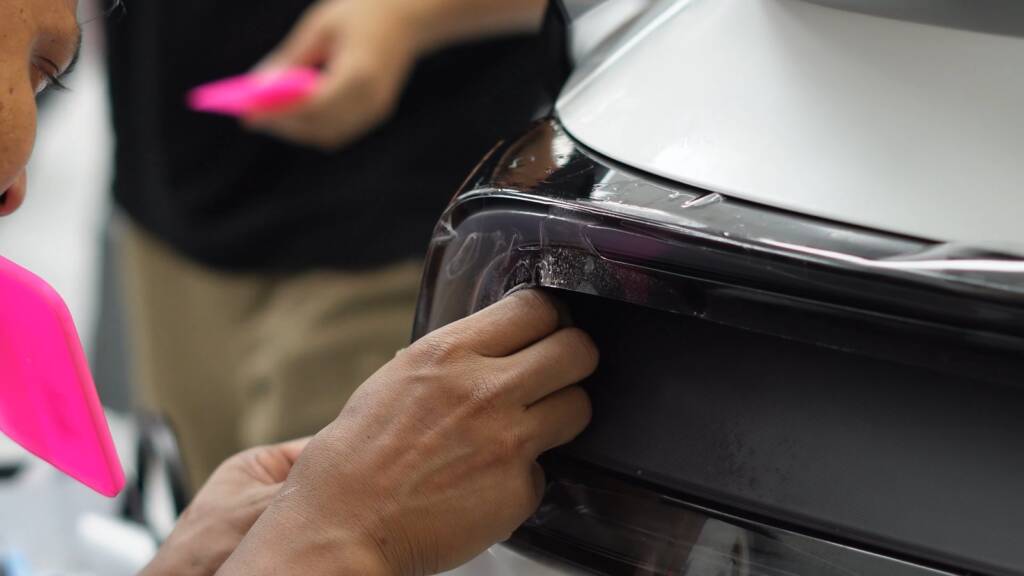 Satin paint protection film being fitted near the rear light of a white Tesla Model Y Performance